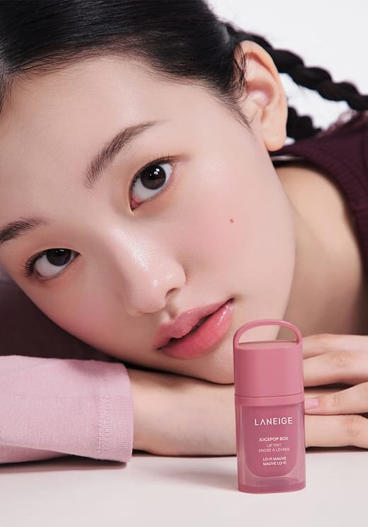 A woman looking straight ahead with LANEIGE JUICEPOP BOX LIP TINT in LO-FI MAUVE on the table