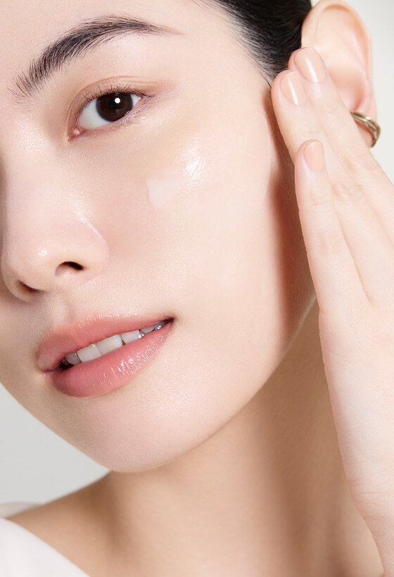 一位女性輕柔地將雪花秀 Ultimate S Infusion Treatment 塗抹於臉頰，展現其透亮質地，突顯產品的保濕功效。