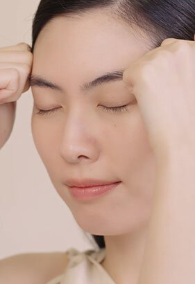 A woman gently massages her forehead with both hands, demonstrating the application technique for Sulwhasoo's Concentrated Ginseng Rejuvenating Cream to achieve firmer, more radiant skin.