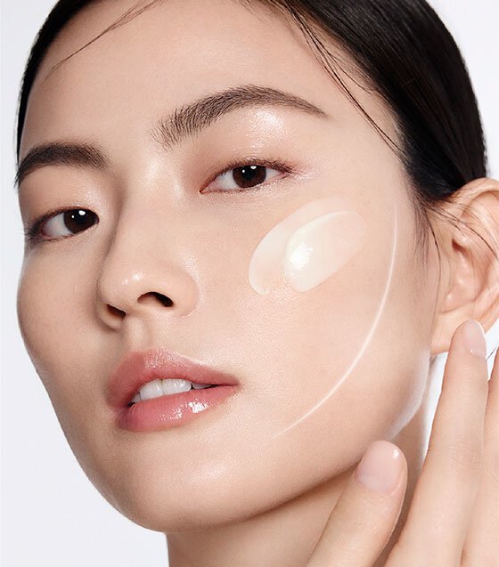 一位女性輕柔地將一坨雪花秀高麗人蔘精華活膚霜塗抹於臉頰，展現乳霜的絲滑質地，同時凸顯其對肌膚的活膚效果。