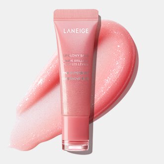 A pink tube of LANEIGE Lip Glowy Balm stands on a vibrant swatch of its shimmering, rosy formula, highlighting the luminous finish of the Stardust Edition.