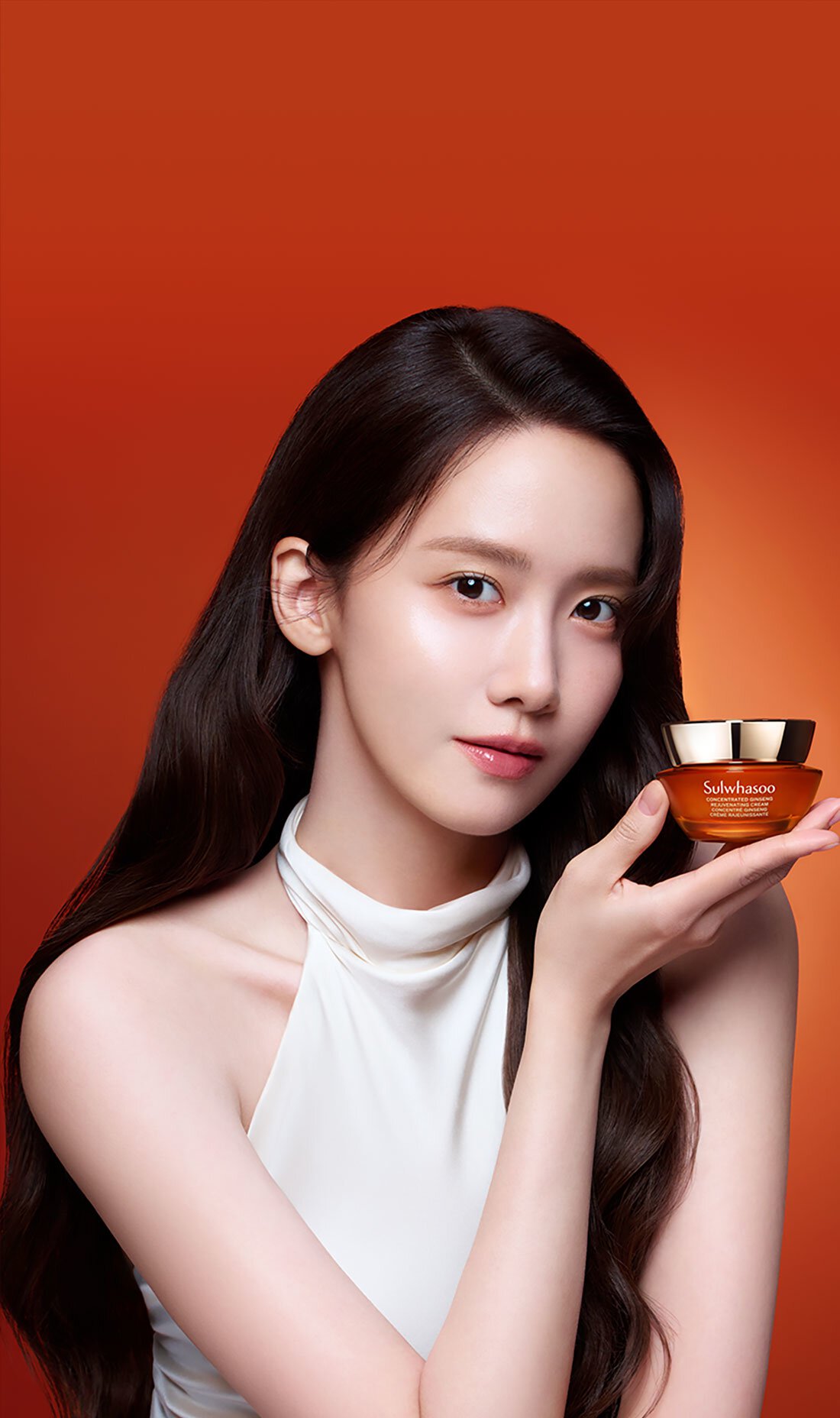 Yoona, with long, dark hair and glowing skin, gently holds a jar of Sulwhasoo Concentrated Ginseng Rejuvenating Cream Rich, showcasing its luxurious texture and promising rejuvenated, plump skin.