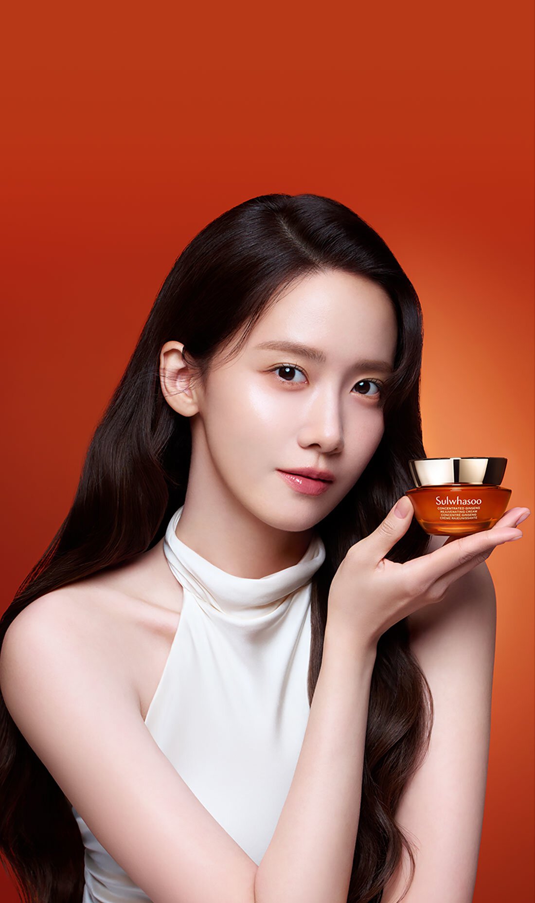 擁有烏黑長髮與透亮肌膚的允兒，輕柔捧著一罐雪花秀人蔘精華活膚霜濃潤版，展現其奢華質地，承諾為肌膚帶來煥活飽滿的觸感。