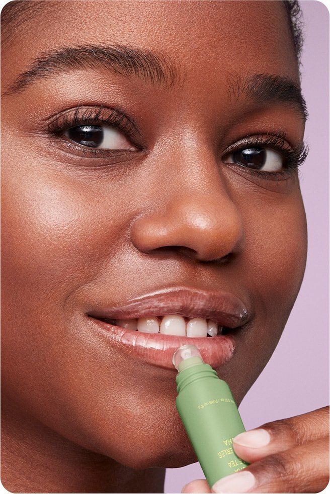 A woman with a bright smile is shown gently applying LANEIGE LIP GLOWY BALM MATCHA BUBBLE TEA to her lips.