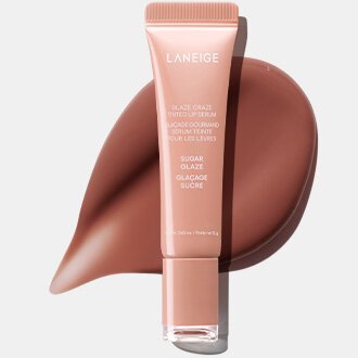 A muted pink tube of LANEIGE GLAZE CRAZE TINTED LIP SERUM in the "Sugar Glaze" shade stands upright on a coordinating, glossy caramel-nude swatch, showcasing the vibrant, glowing finish characteristic of Laneige's Lip Glowy Balm Stardust Edition.