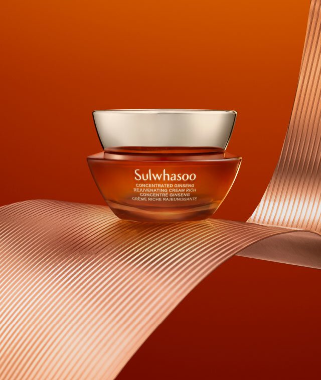 A jar of Sulwhasoo Concentrated Ginseng Rejuvenating Cream Rich rests on a copper-colored ribbon against a burnt orange background, showcasing its rich, luxurious texture designed to plump skin and reduce the appearance of fine lines and wrinkles.