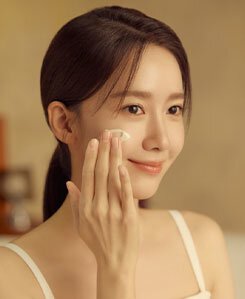 允兒帶著溫柔微笑，塗抹雪花秀人蔘活膚精華霜濃潤版，展現其乳霜般質地，同時凸顯產品對她光彩照人、健康肌膚的活膚效果。