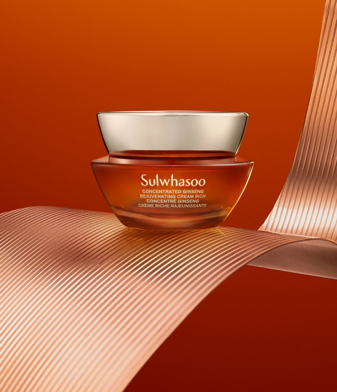 A jar of Sulwhasoo Concentrated Ginseng Rejuvenating Cream Rich sits elegantly on a copper-colored ribbon, showcasing its rich, amber-toned cream that promises to plump skin and reduce the appearance of fine lines and wrinkles.
