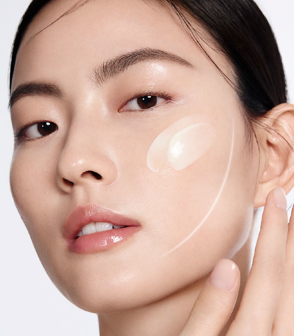 一位女性輕柔地將一坨雪花秀高麗人蔘濃萃活膚霜塗抹於臉頰，展現乳霜的奢華質地及其豐盈肌膚、淡化細紋與皺紋的潛力。