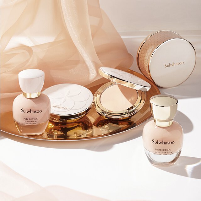 An open Sulwhasoo Perfecting Powder compact, revealing its light-toned pressed powder, sits elegantly on a reflective gold tray with various Perfecting Foundations, showcasing the comprehensive range for a flawless, skin-caring finish.